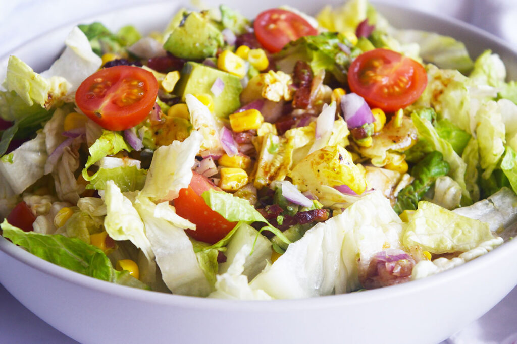 Front, horizontal view of a white bowl holding a Loaded Bacon Salad.