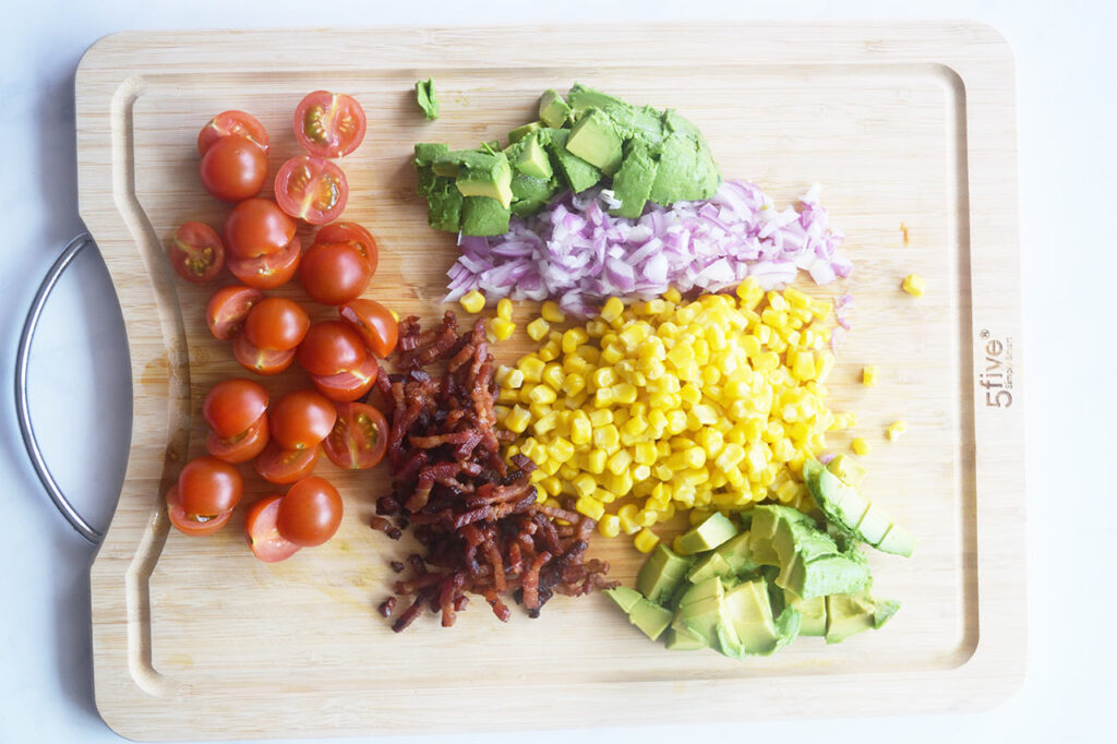Overhead focus. A cutting board with chopped vegetables and bacon bits on it.