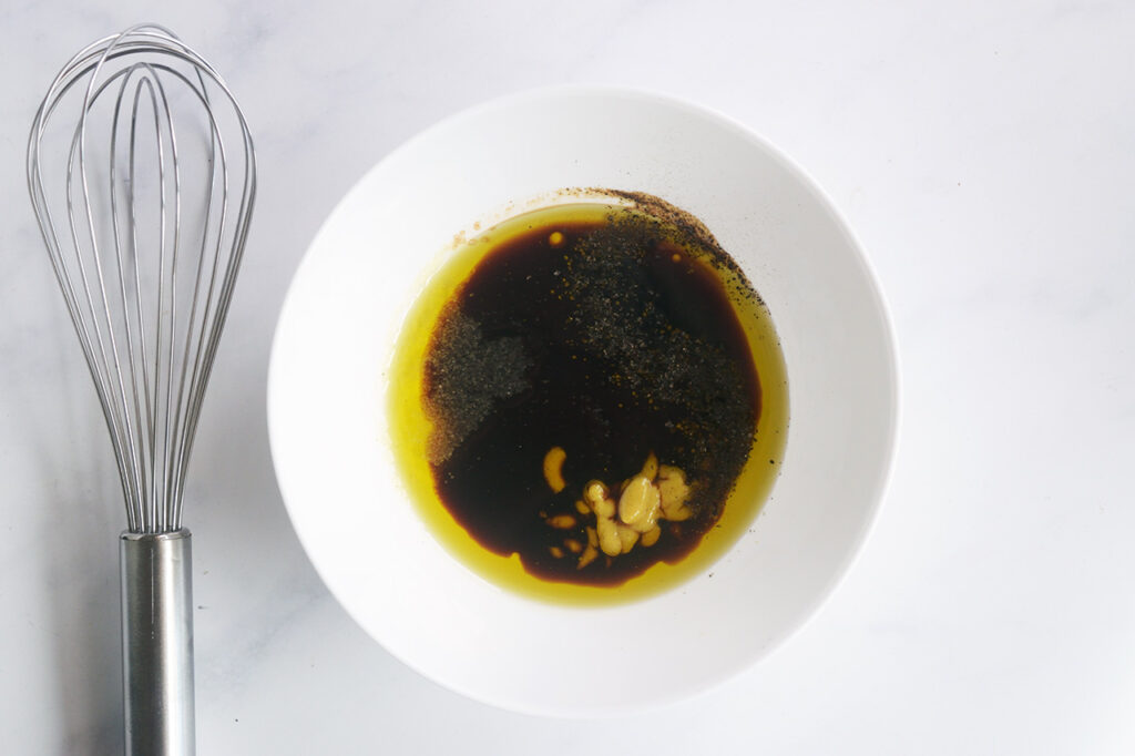 Overhead focus. White bowl with dressing ingredients. A whisk lays to the left.