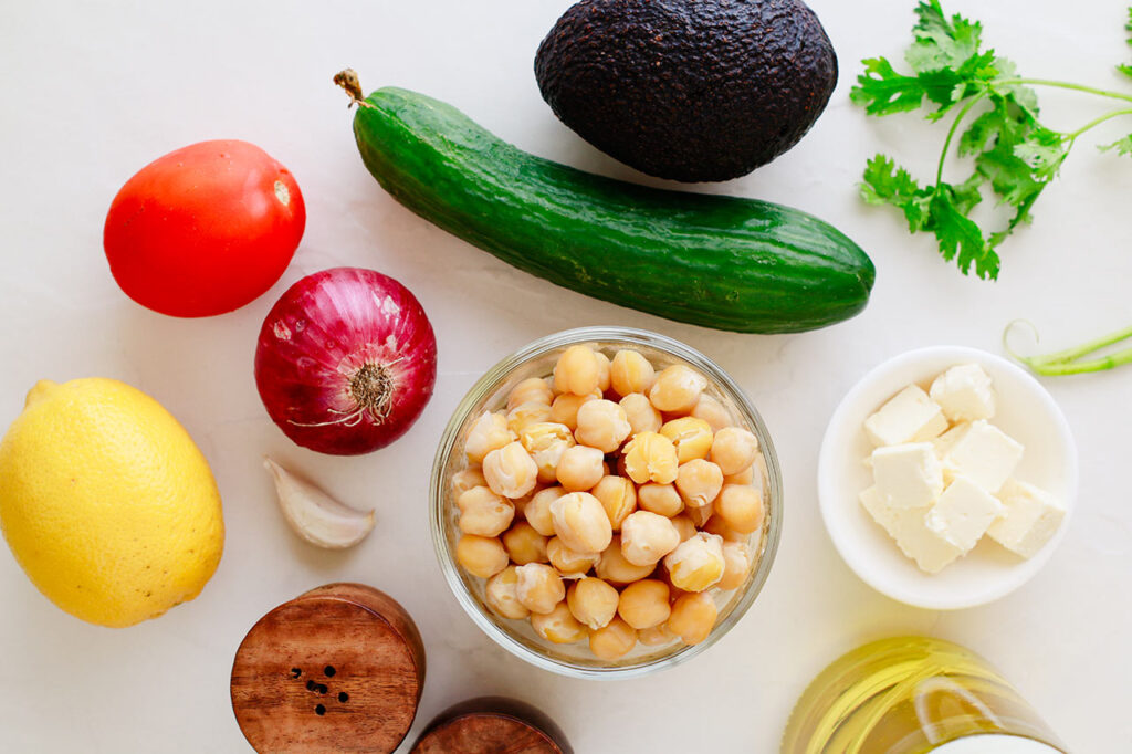Ingredients for this Mediterranean Chickpea Salad gathered on a white surface.