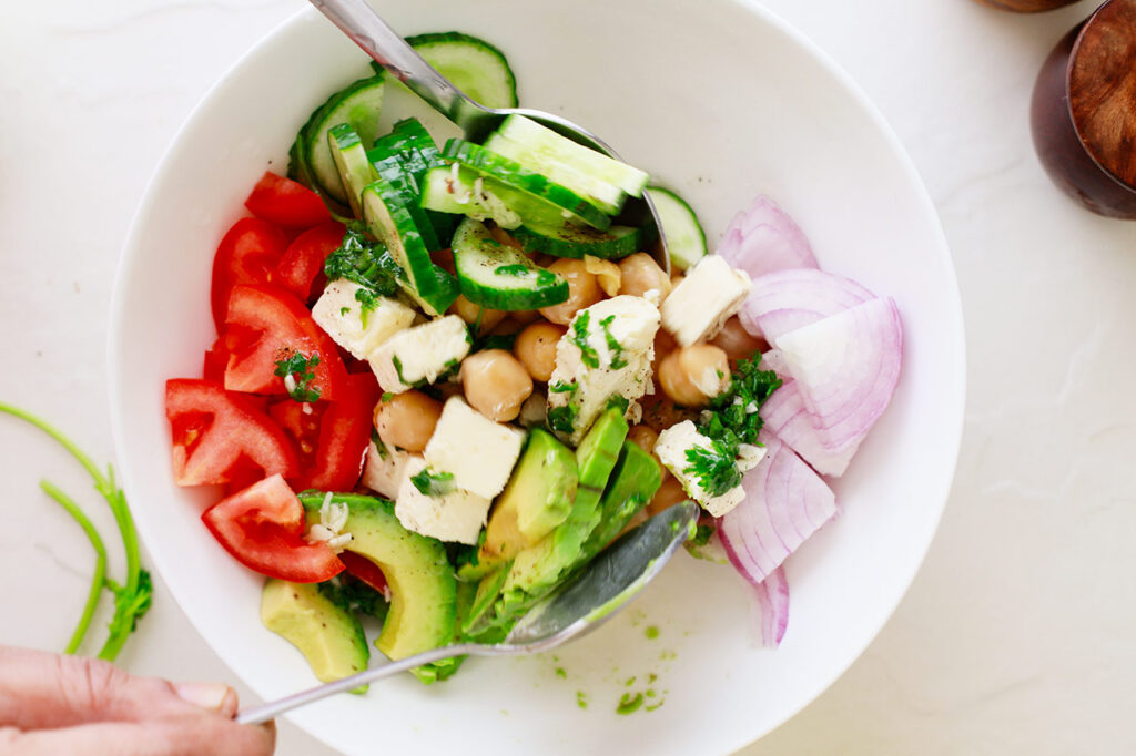Tossing a Mediterranean Chickpea Salad in a white mixing bowl.