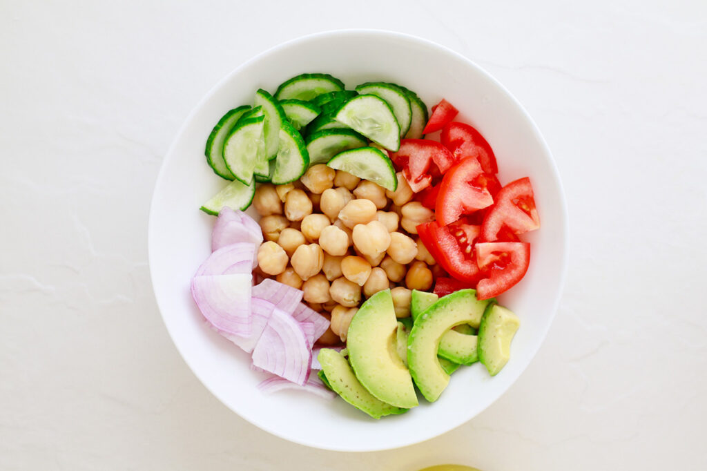 Salad ingredients chopped, and placed in a white mixing bowl.