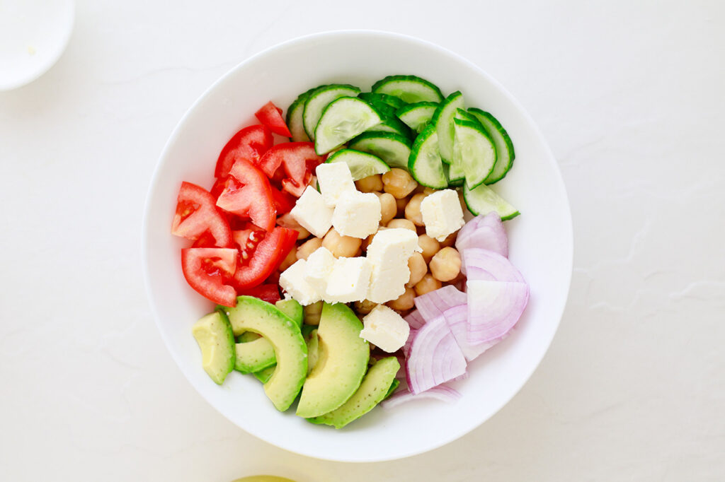 Cheese added to the salad in a white mixing bowl.