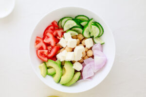 Cheese added to the salad in a white mixing bowl.