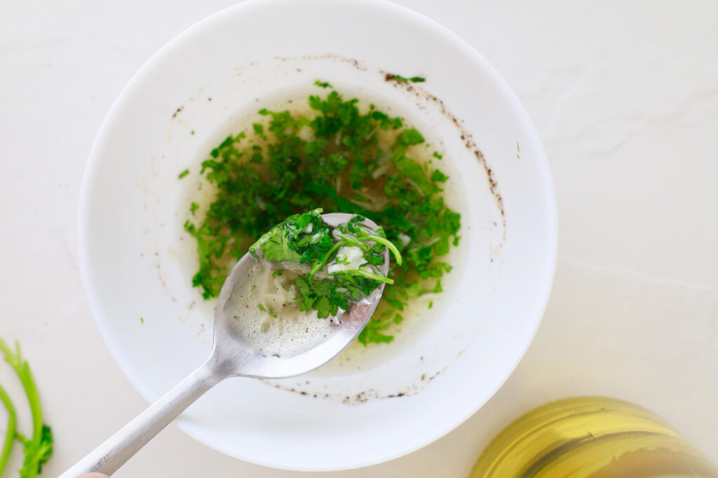 A spoon lifts a bit of dressing out of a mixing bowl.
