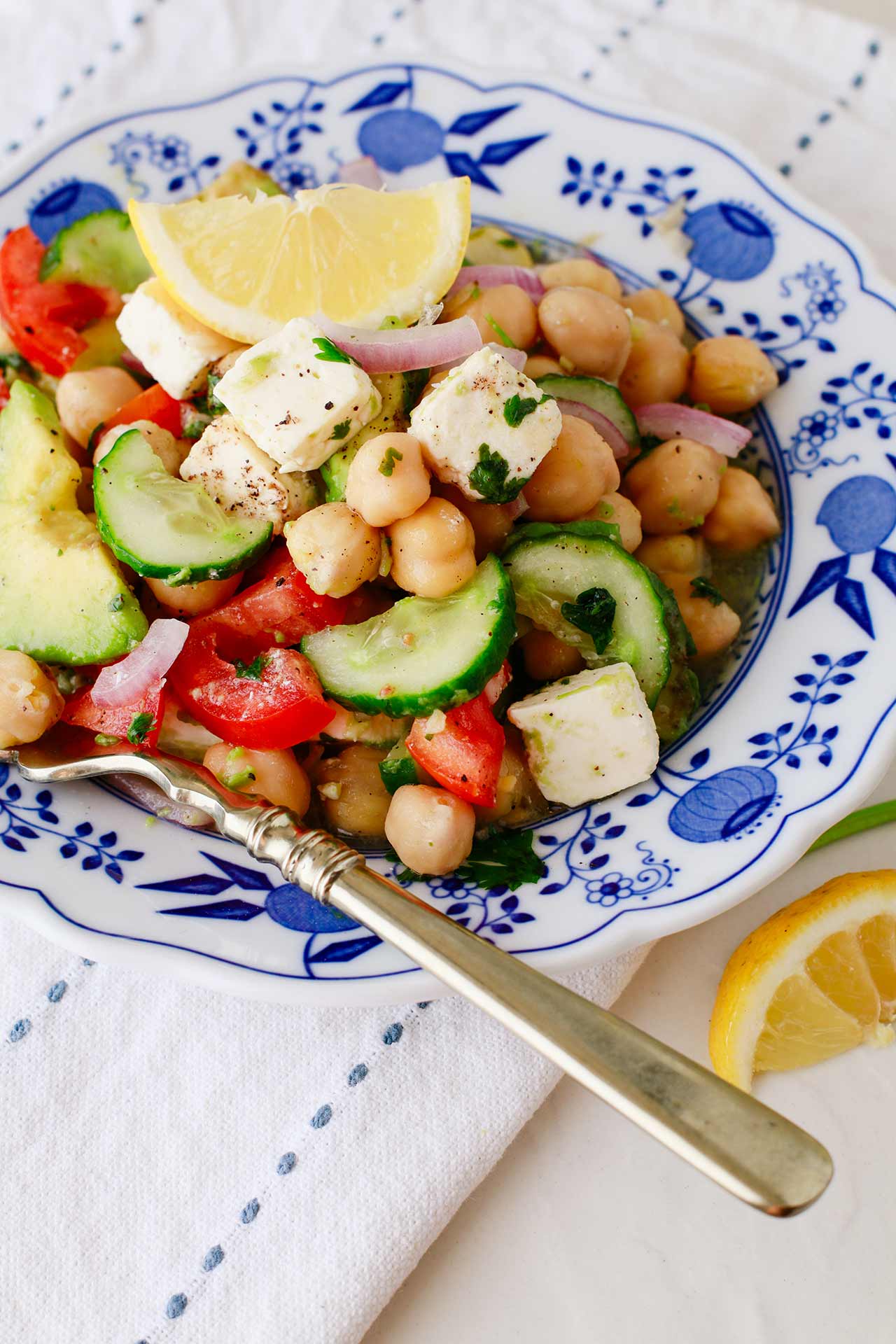 A decorative bowl full of Mediterranean Chickpea Salad sits on some white and blue linen.
