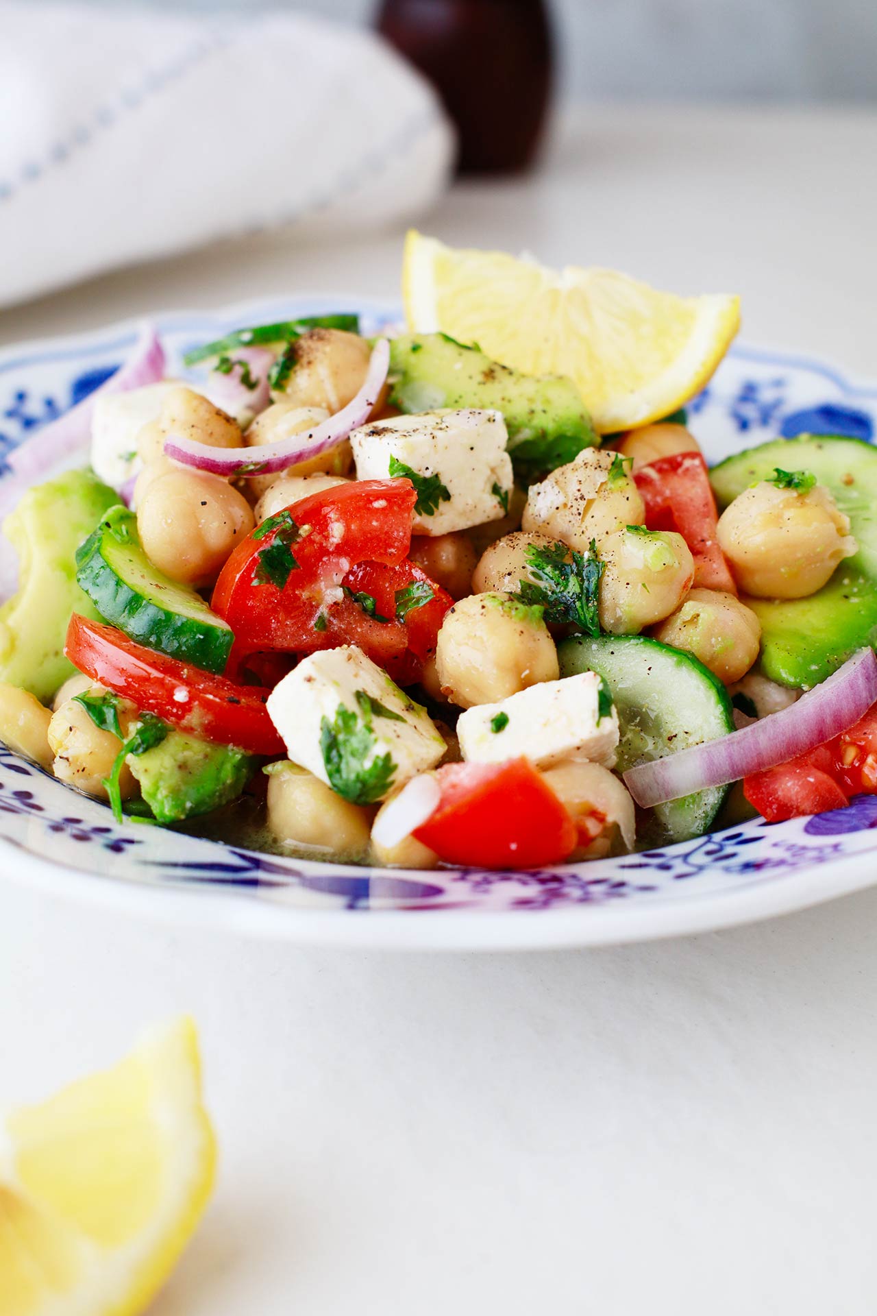 A bowl of Mediterranean Chickpea Salad on a white surface with fresh lemon wedges.