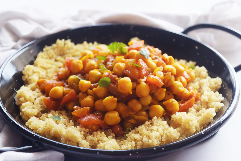 Front view of a black pan filled with a bed of quinoa topped with Moroccan Chickpea Stew and garnished with fresh herbs.