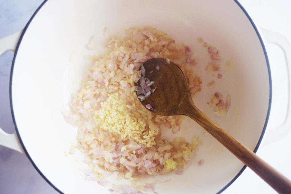 Minced garlic added to onions and ginger in a Dutch oven.