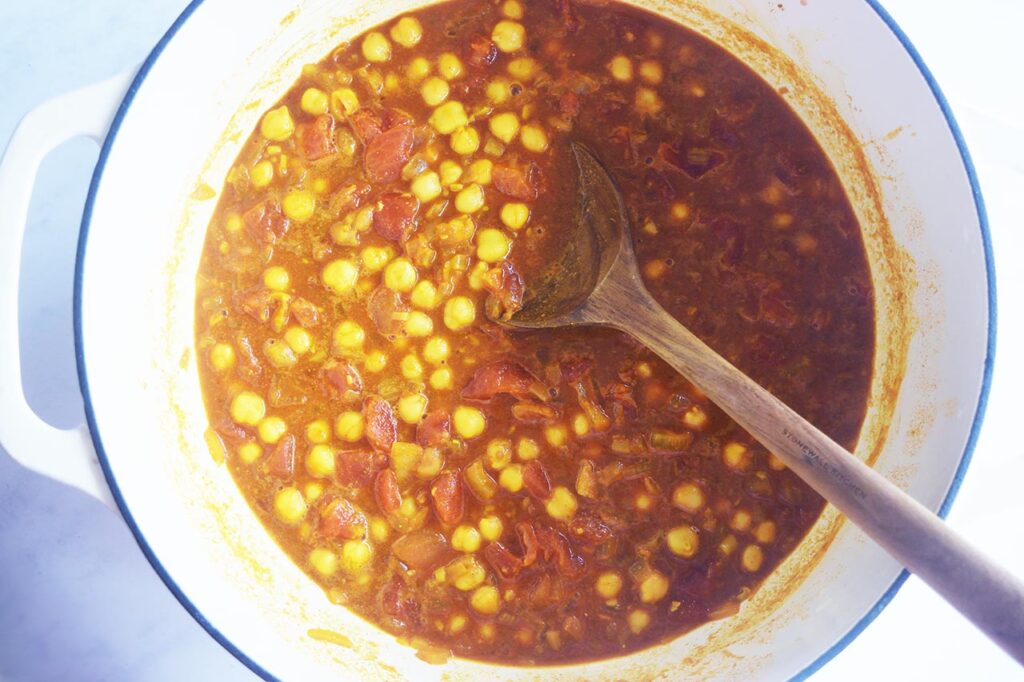 Broth and tomatoes added to a Dutch oven along with chickpeas.
