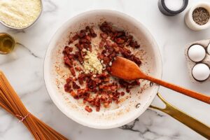 Cooked bacon bits in a skillet with fresh, minced garlic.