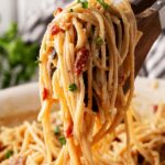 Tongs lift up a serving of Pasta Carbonara from a skillet.