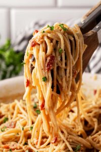 Tongs lift up a serving of Pasta Carbonara from a skillet.