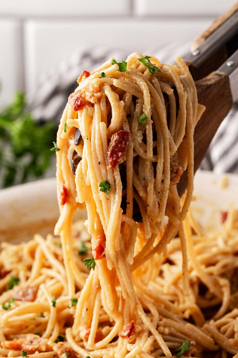Tongs lift up a serving of Pasta Carbonara from a skillet.