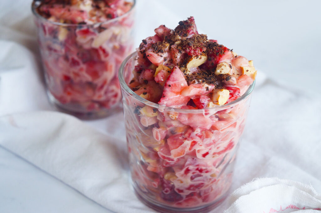 Two glass cups of Strawberry Salad garnished with chocolate shavings on a white background.