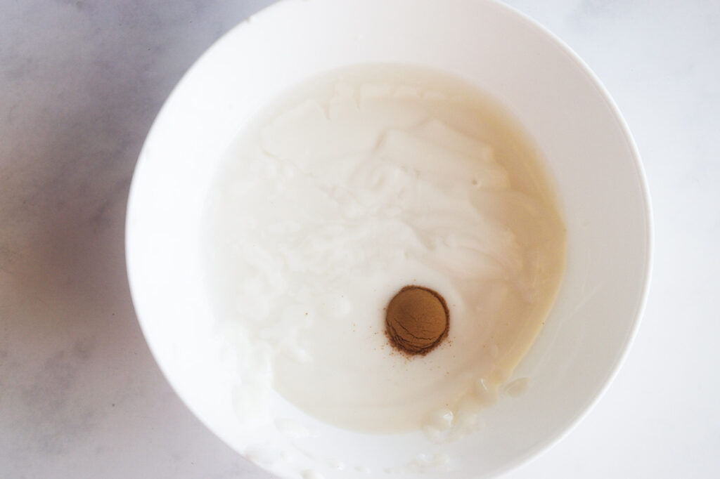 Yogurt with sweetener and ground cinnamon sits unmixed on a white background.