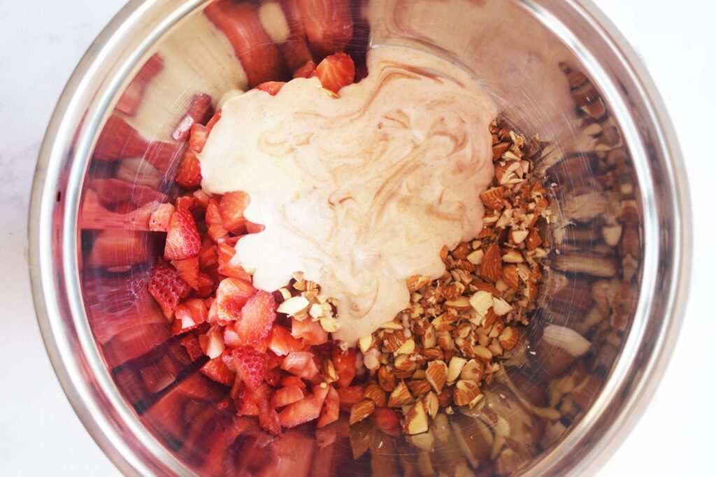 Dressing added to strawberries and almonds in a mixing bowl.