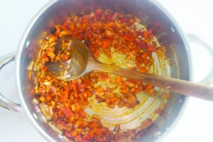 Sautéed vegetables in a pot with a wooden spoon.