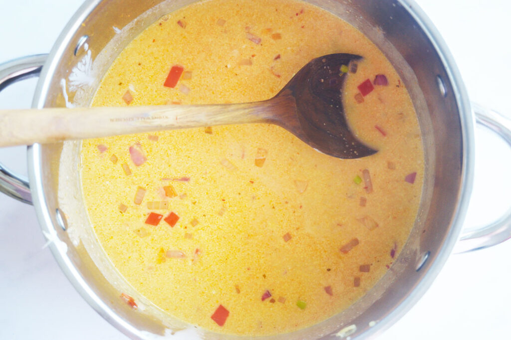 Coconut milk and broth added to a pot of sautéed vegetables.