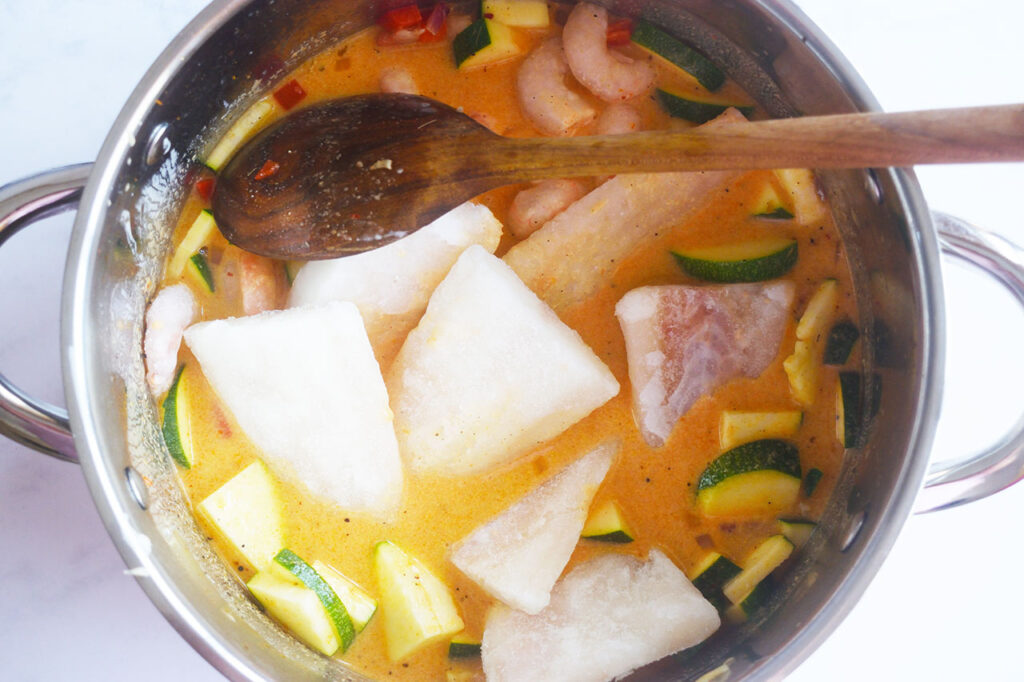 Frozen cod and shrimp added to a pot of broth and vegetables.