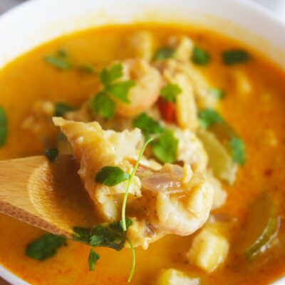 A spoon lifts up a serving of Thai curry with shrimp and cod from a white bowl.