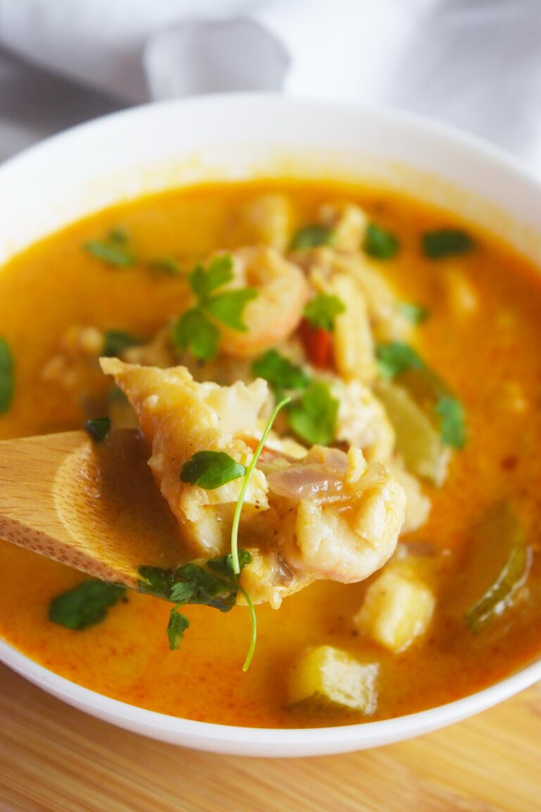 A spoon lifts up a serving of Thai curry with shrimp and cod from a white bowl.