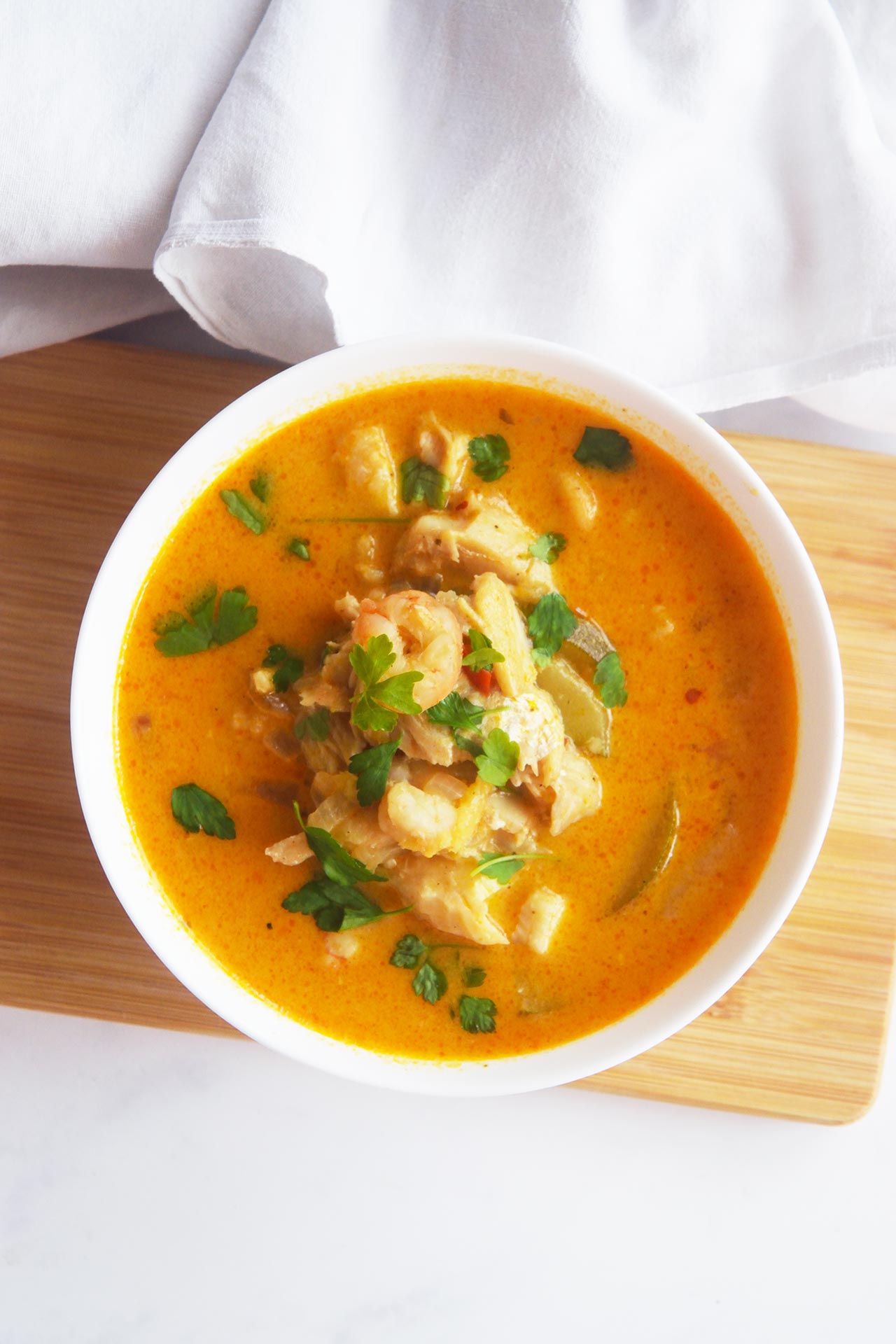 Overhead focus. Thai curry with shrimp and cod garnished with green herbs in a white bowl.