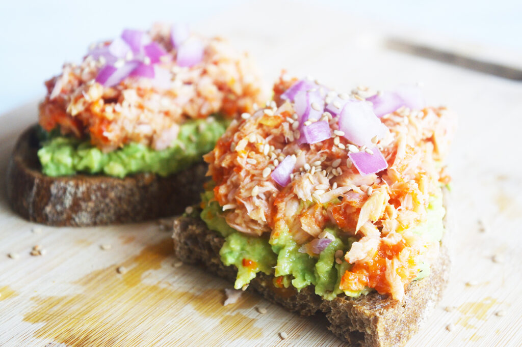 Front view of two pieces of tuna avocado toast on a wood surface.