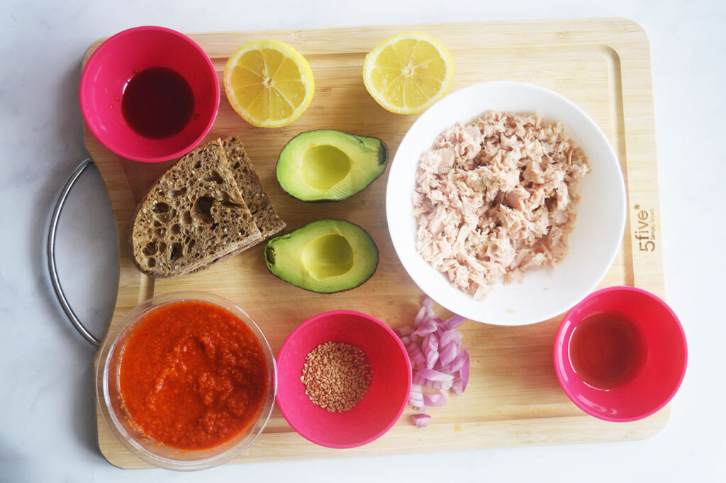 Ingredients for a Tuna Avocado Toast sitting on a wood cutting board.