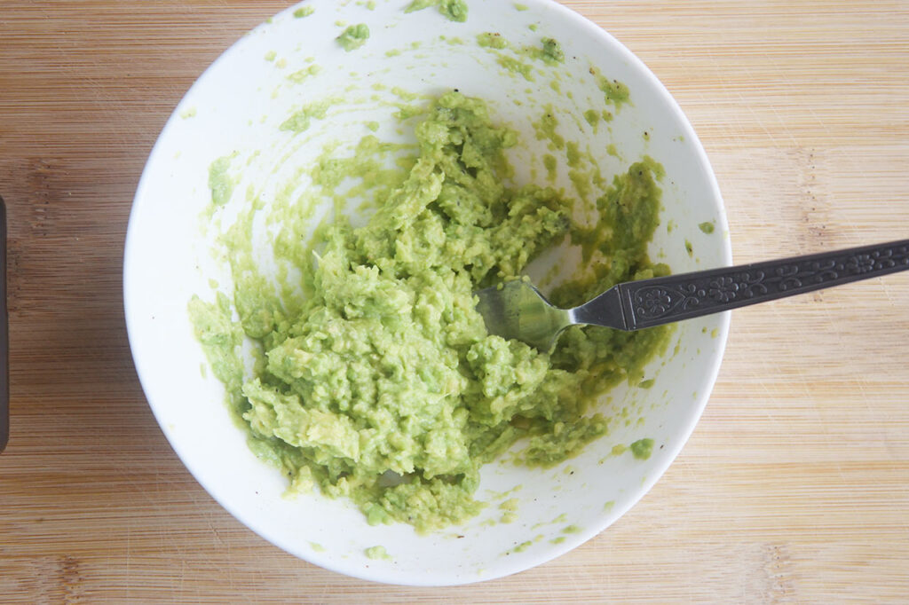 Mashed avocado with lemon juice and salt in a white bowl.