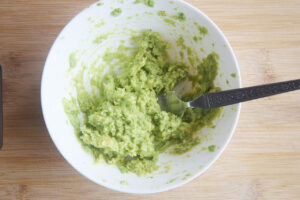 Mashed avocado with lemon juice and salt in a white bowl.