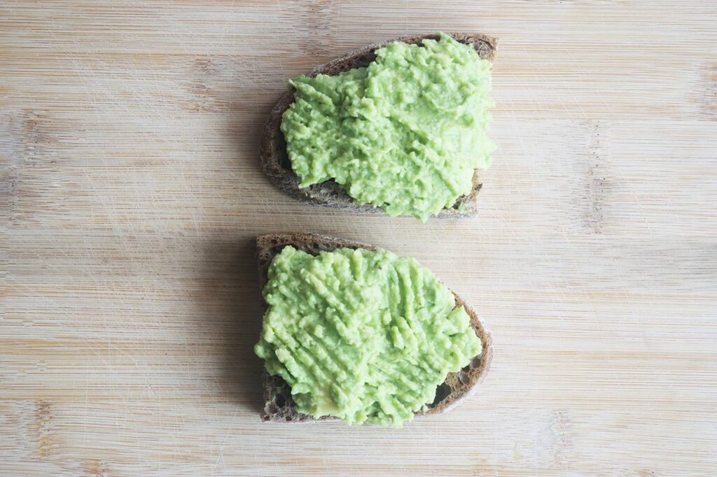 Mashed avocado spread over two slices of toast.