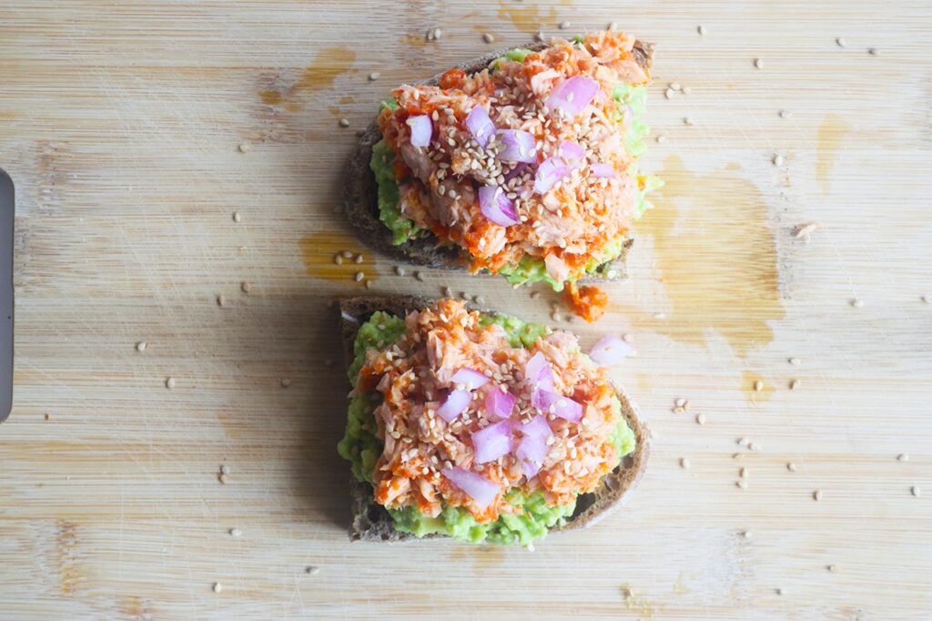 Avocado toast topped with Sriracha tuna, chopped red onions, and sesame seeds. Overhead focus.