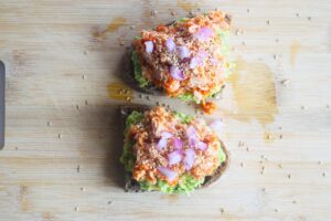 Avocado toast topped with Sriracha tuna, chopped red onions, and sesame seeds. Overhead focus.