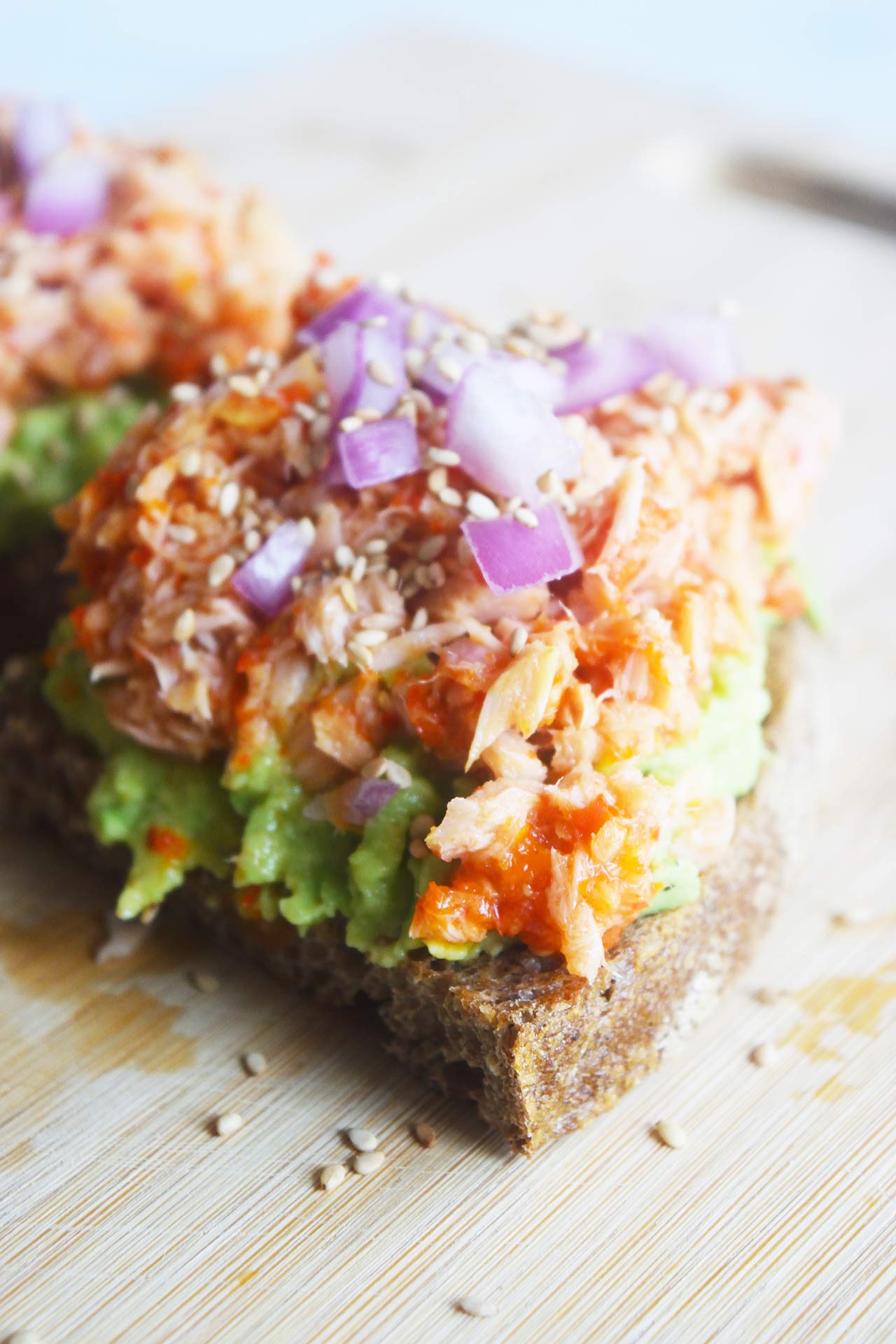 Side view of a slice o tuna avocado toast on a wood cutting board.