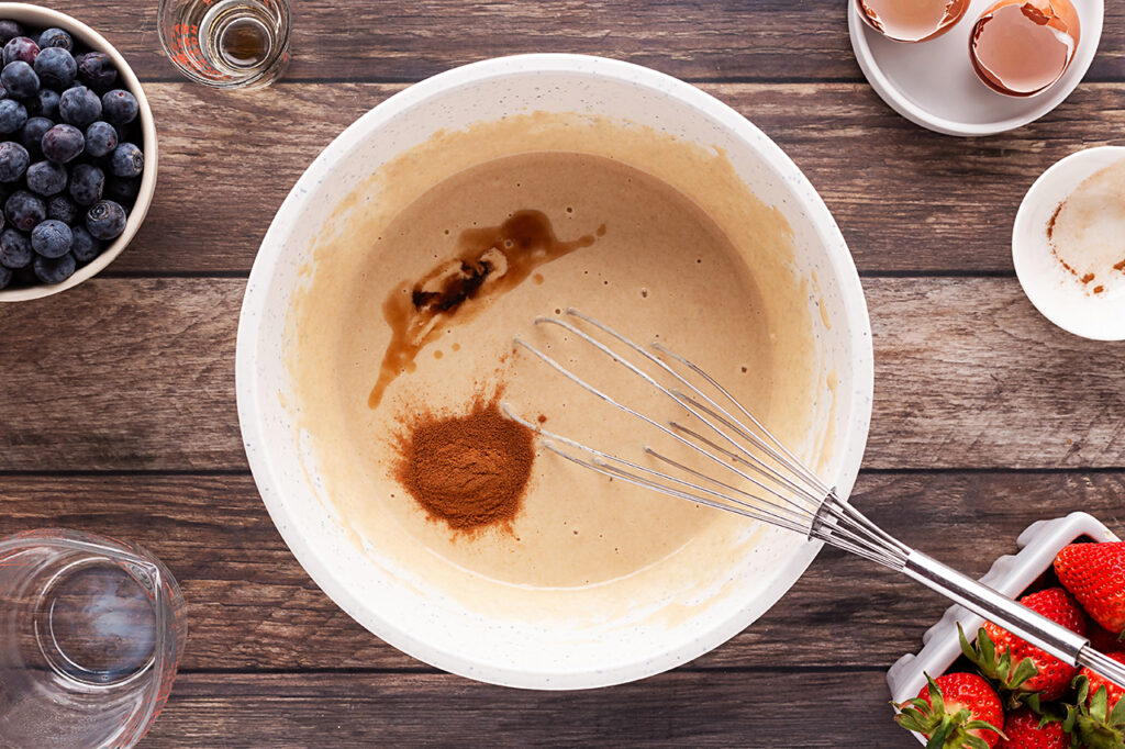Vanilla and cinnamon added to milk, flour, and eggs in a mixing bowl.