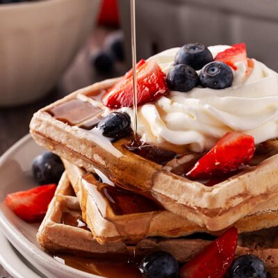 Pouring syrup over garnished waffles on a plate.