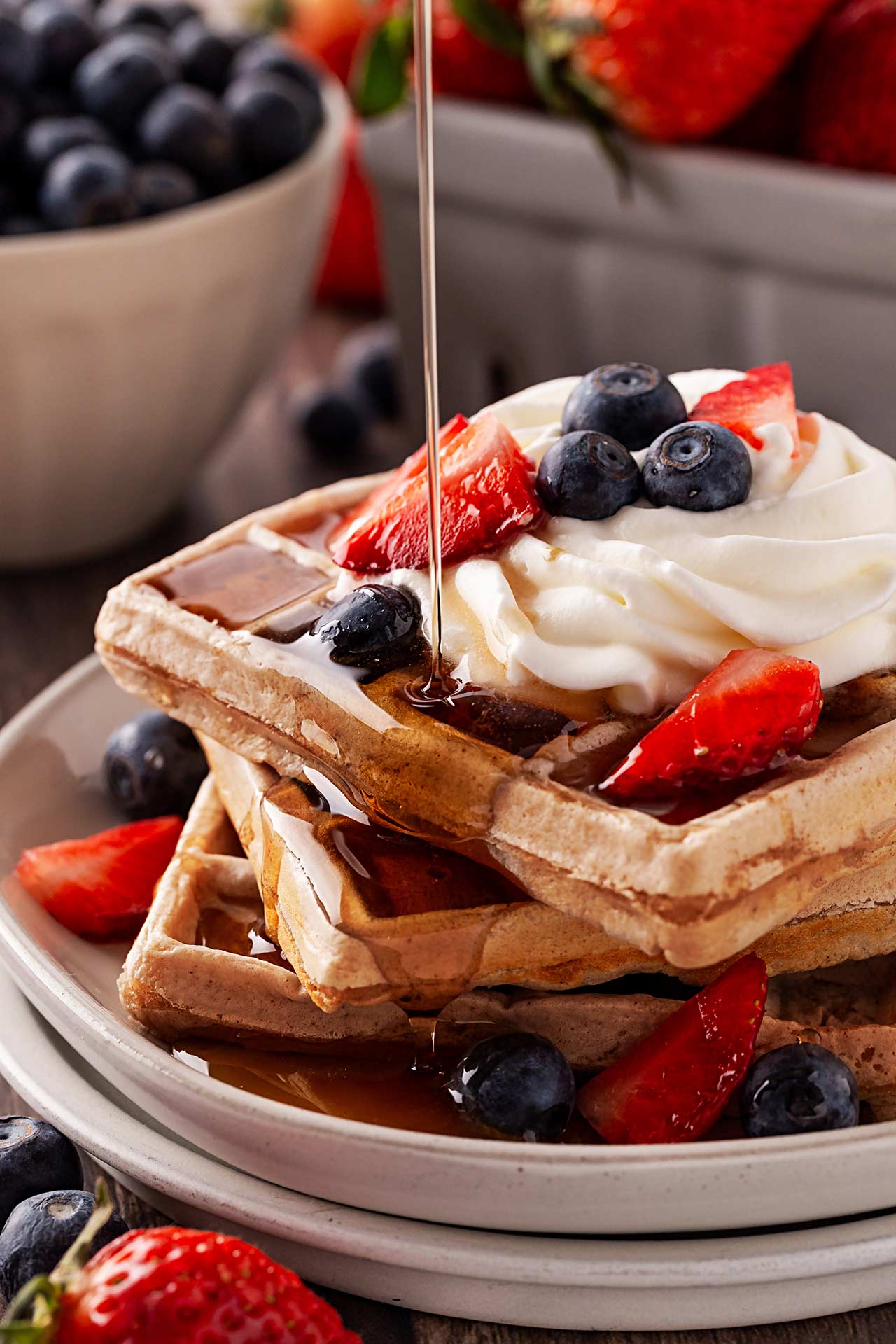 Pouring syrup over garnished waffles on a plate.
