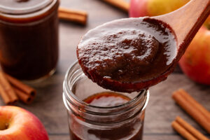A wooden spoon holds a spoonful of apple butter over an open jar.