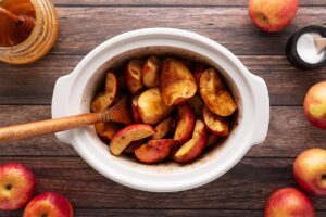 Apples in a white slow cooke crock, stirred until coated with spices and sweeteners.