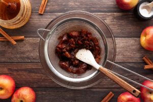 Pressing cooked apples through a fine-meshed sieve over a bowl.
