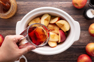 Adding apples and apple juice to a slow cooker crock.