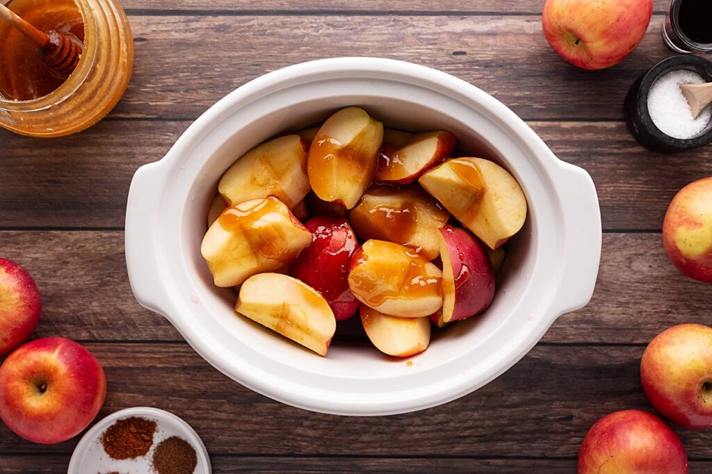 Honey poured over cut apples in a slow cooker crock.