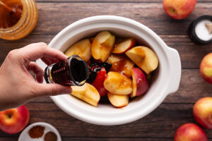 Pouring molasses over cut apples in a slow cooker crock.