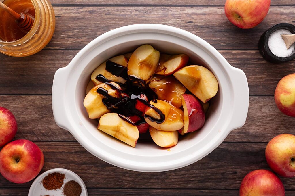 Molasses drizzled over cut apples in a white crock.