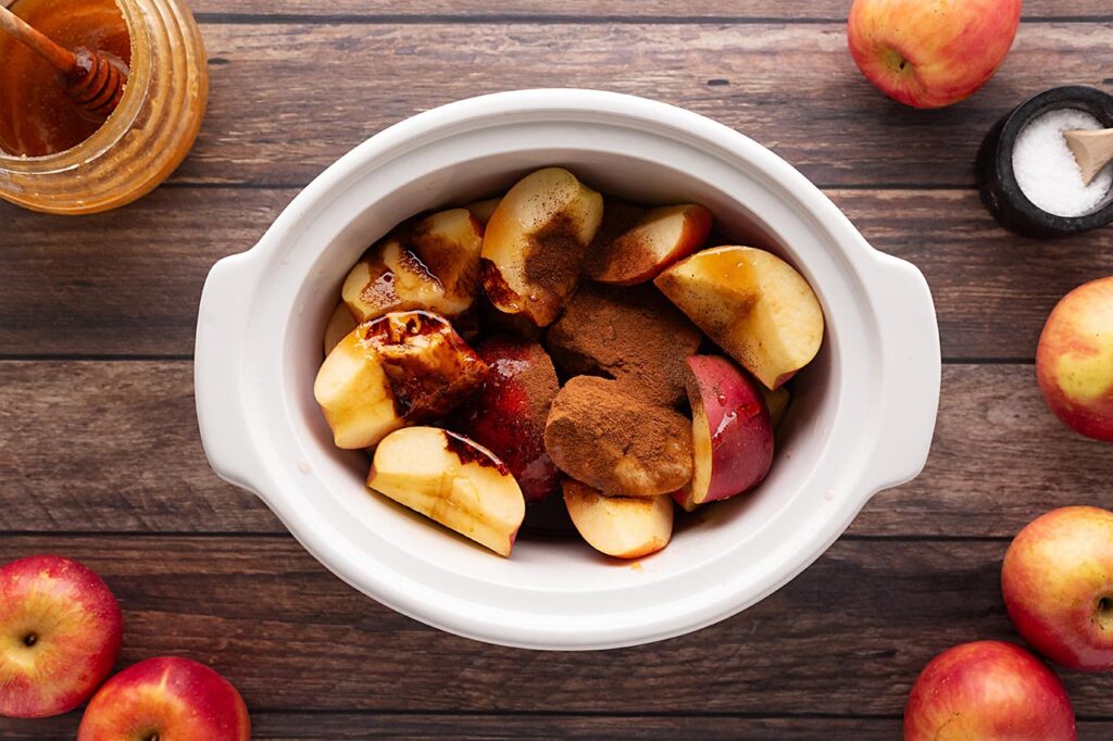 Spices added to cut apples in a white slow cooker crock.