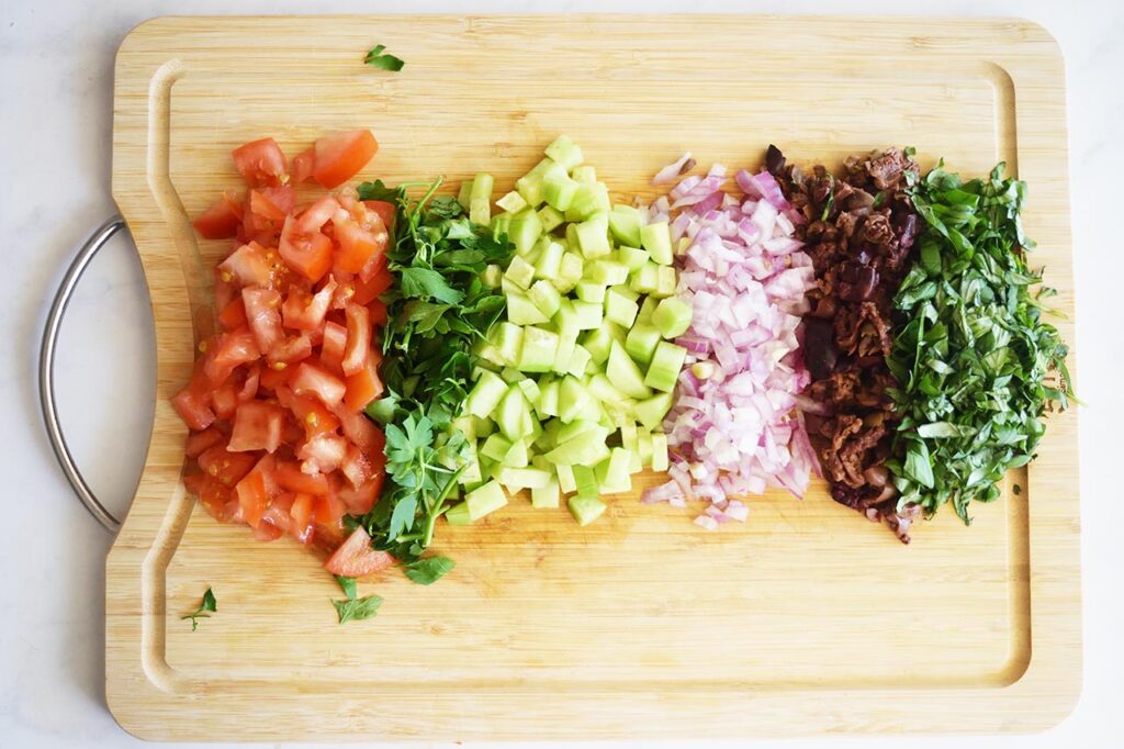 Chopped herbs and veggies on a wood cutting board. Overhead focus.
