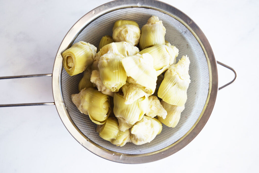 Drained artichoke hearts in a strainer. Overhead focus.