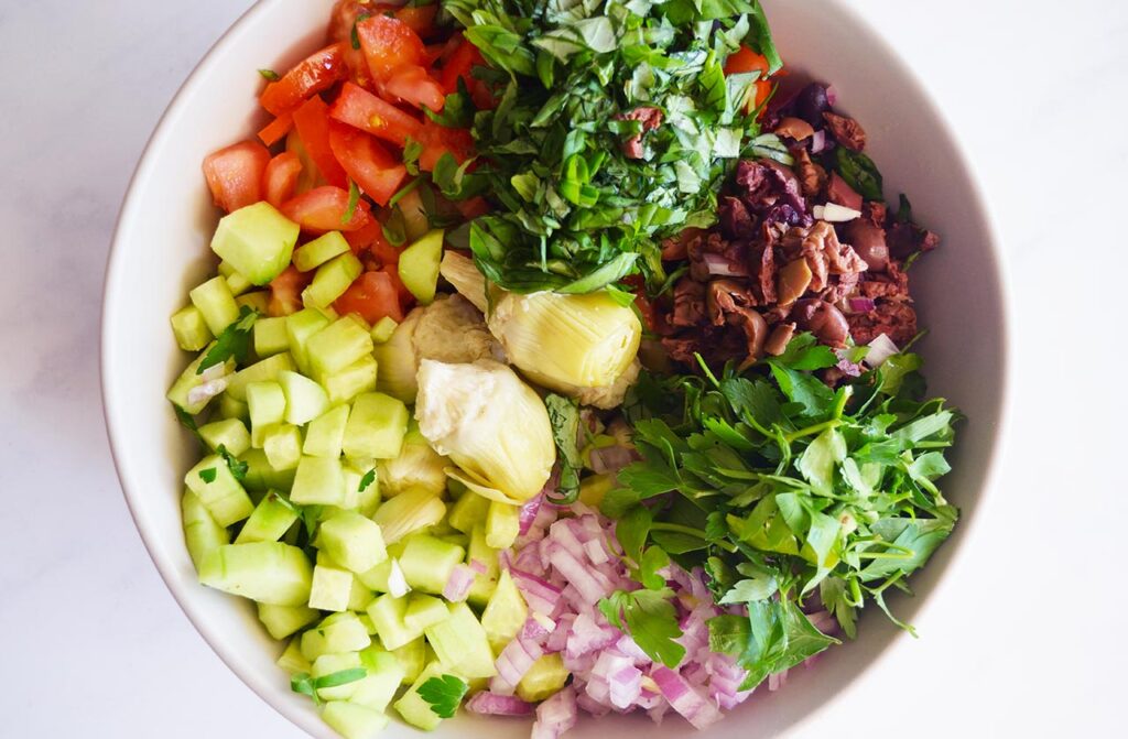 Artichoke Salad ingredients in a white mixing bowl, unmixed. Overhead focus.