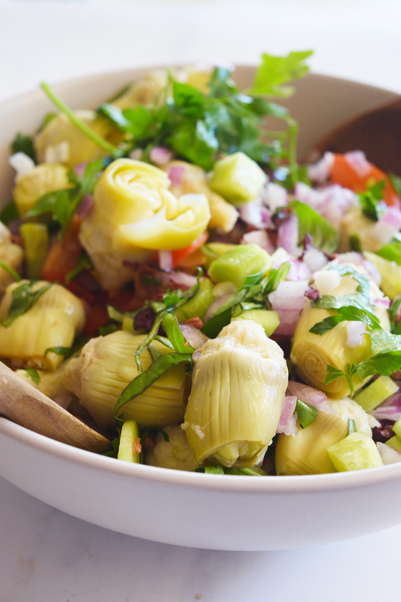 Front view of a white bowl filled with Artichoke Salad.
